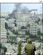 An Israeli soldier looks out over Ramallah as smoke rises over the city