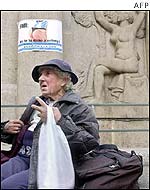 Old woman sitting under anti-IMF poster
