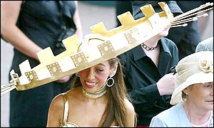A woman wears a flamboyant golden hat next to the Royal enclosure