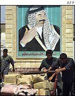 Iraqi workers pass a portrait of Iraqi leader Saddam Hussein 