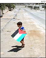 A boy alone in the street with a Palestinian flag