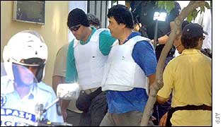 Vassilis (left) and Christodoulos Xiros (right, in flak jackets) come out of the prosecutor's office escorted by police