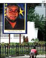 Polio victim passes poster of Laurent Kabila in Kinshasa