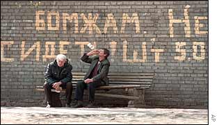 Men drinking on bench in front of sign warning of fine for drinking in public