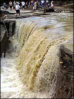 People stand by a waterfall caused by torrential rains in the village of Shirokaya Balka