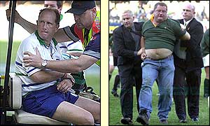 Referee David McHugh (left) is taken off the field injured following an attack by a supporter, who is escorted from the field
