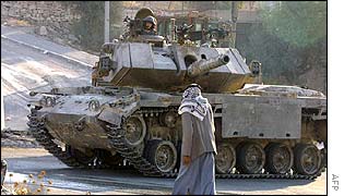 A Palestinian man walks past an Israeli tank 