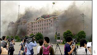 Journalists watch a smoking building 'bombed' by enemy planes