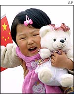 A girl cuddles a toy bear while waving the national flag