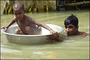 Man takes his son away from floodwaters in a household utensil, near Dhaka 