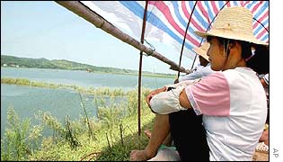 Locals watch a dyke on a flood river feeding Dongting