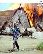 Man from migrant workers district in Abidjan walks past blazing home