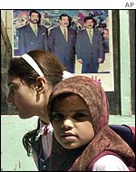 Iraqi children pass a political poster