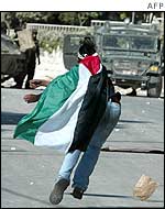 Palestinian boy wearing the Palestinian flag throws stones at Israeli tank