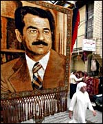 Man walks under portrait of Saddam Hussein