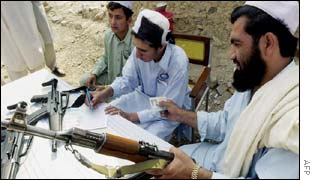 An armed tribal man (r) presents his identity card to an election official 
