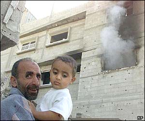 Palestinian residents stand by a burning building after it was hit by a tank shell 