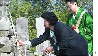 Japanese kidnapping victim Hitomi Soga adjusts her family tombstone as a Buddhist priest looks on, Sado Island, northern Japan,