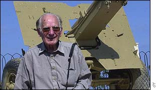 Michael Coustant, a British captain during WWII smiles in front of a British 17 PDR Antitank gun
