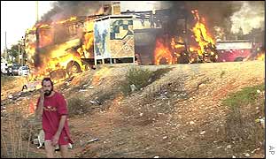 A man stands near the burning bus