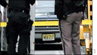 Law enforcement officers, watch as a car bearing New Jersey license plate number NDA-21Z is pushed into a garage 