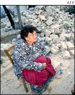 An old woman sits near the remains of her house