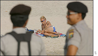 Indonesian police watch over a Bali beach as a tourist sunbathes 