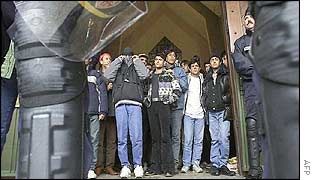 Migrants outside the church, framed by riot police