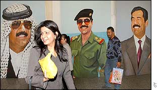 An Iraqi woman walks past portraits of Saddam Hussein