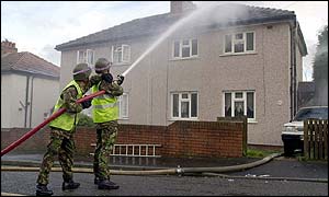 Army firefighters spraying house with water