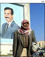 Iraqi man stands in front of portrait of Saddam Hussein 