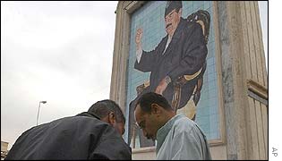 Iraqi men stand underneath a portrait of Saddam Hussein in Baghdad