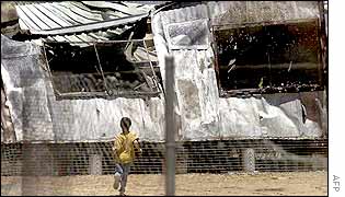 A young boy wanders through the burnt out ruins of the Woomera detention centre for illegal immigrants after it was deliberately set ablaze by the detainees 18 December 2001. 