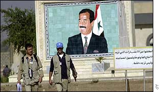 UN inspectors walk past mural of Saddam Hussein