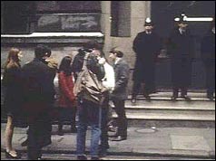 Group of students wait outside, as police guard the entrance 