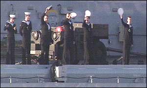 Troops on the Ark Royal wave their hats in the air