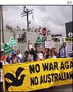 Protestors gather outside the Garden Island Naval Base in Sydney as HMAS Kanimbla, back, prepares to sail 