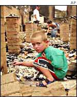 A young boy looks through the rubble of his home