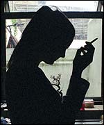 A silhouette of a woman smoking by a window