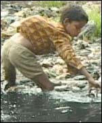 Boy picks bottle from a factory sewer for recycling