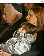 Rona Ramon, wife of Israeli astronaut Ilan Ramon holds their daughter Noah while sitting alongside Israeli Prime Minister Ariel Sharon during a state ceremony, 10 February 2003
