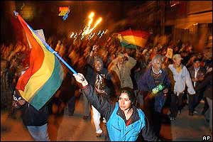Woman waves huge Bolivian flag as protesters chant and raise their fists behind her