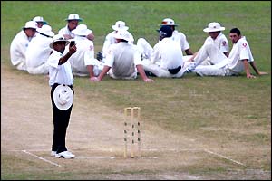 An umpire checks his light metre as the England team sit and wait