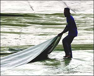 A groundsman covers the pitch as the rain pours down