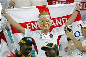 An England fan with a mask of the Queen Elizabeth on holds a flag of St George aloft