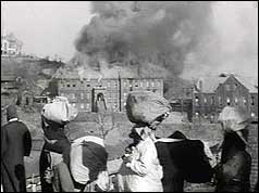 North Koreans with luggage on heads and burning building in background