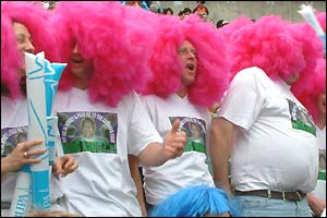 A group of fans on tour wear bright pink wigs in the stands