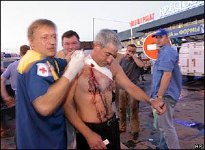 A wounded man with blood in his chest is helped by an ambulance worker