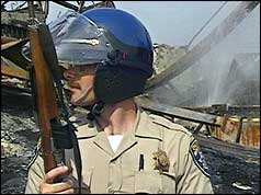 Officer in riot gear in front of damaged building