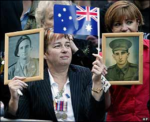 Members of the public hold up pictures of family members as they watch the annual Anzac Day parade through the streets of Sydney on Sunday